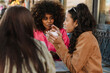 © Drobot Dean - A woman is holding a cup and talking while sitting at a table next to two female friends