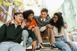 © Drobot Dean - A group of four students sit on a table and bench and laugh while leaning on each other