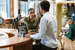 © Drobot Dean - A female worker is talking to a male worker who is typing on a laptop while they are sitting at a table