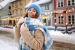 © maxbelchenko - Portrait of joyful woman in cozy clothes strolling along snowy streets of city against backdrop of bright lights. A beautiful woman enjoys winter day outdoors. Concept: tourism, holiday, lifestyle.