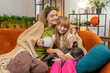 © Andrii Iemelianenko - Mother and daughter with French bulldog at home pour tea share sip cover with blanket breathe slow. Woman and girl with dog on sofa relax hug smile watch calm screen mute sound enjoy warm family rest