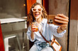 © maxbelchenko - Happy woman in sunglasses and holding refreshing drink takes selfie with her phone on sunny day. Beautiful woman on cafe terrace blogs, enjoys coffee. Concepts of blogging and relaxation.
