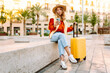 © maxbelchenko - Cheerful woman with a yellow suitcase and phone admires city's architecture. A tourist in hat and with backpack strolls along the sunny streets of city. Concepts of tourism, weekends.