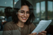 © ZANNATUL NAYIM - Smiling woman with glasses reading document inside a coffee shop