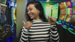 © Krakenimages.com - Young woman in striped top gives thumbs up at slot machines in casino under colorful lights; celebration luck excitement winning.