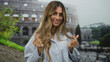 © Krakenimages.com - Young blonde woman makes finger heart gesture with both hands in front of sunlit colosseum; affection joy travel romance.
