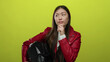 © Krakenimages.com - Woman pondering holding helmet in red jacket against vibrant yellow background showing thoughtful expression.