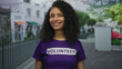 © Krakenimages.com - Smiling young woman volunteer in a purple shirt outdoors on a vibrant street illustrating community and youth engagement.