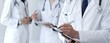 © rogerphoto - Doctor writing on a clipboard during a medical team discussion, collaborating on patient care, documentation, and healthcare strategy in a clinical setting