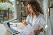 © Miljan Živković - Woman working remotely with laptop analyzing home office paperwork
