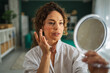 © Miljan Živković - Woman doing morning beauty routine holding a mirror