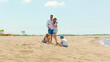 © Videophilia - Happy family of four on a sunny sandy beach, parents embracing while kids build sandcastles and play at the water’s edge, enjoying summer vacation together