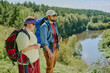 © AnnaStills - Caucasian young girl with Down syndrome and Caucasian young man standing on grassy riverbank carrying backpacks, looking at scenic landscape, enjoying outdoor hiking adventure together in nature