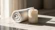 © Platon - Serene spa setting with lit candle and rolled white towel on marble.A serene and clean spa or bathroom detail shot featuring a thick, rolled white towel next to a lit pillar candle on a bright marble