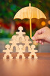 © sommart - Hand holding wooden umbrella over stacked wooden people figures, symbolizing team protection, group insurance, organizational safety, and support structure concept.