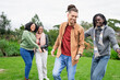 © Wavebreak Media - Diverse friends wearing scarves and jackets playing chase game on grassy park lawn under cloudy sky