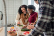© Wavebreak Media - Diverse friends seasoning vegetables, mixing greens and slicing cucumber on kitchen island