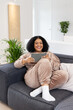 © Wavebreak Media - Mid adult African American woman wearing tracksuit sitting on couch in living room holding tablet