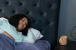 © Wavebreak Media - African American woman lying on bed by nightstand holding smartphone and mug, copy space