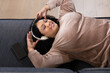 © Wavebreak Media - Mid-adult woman lying at home on sofa listening on white headphones and resting smartphone nearby