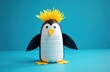 © Vadym - Recycled yogurt bottle craft penguin stands on blue background. Cute handmade bird art project uses plastic bottle, paper, googly eyes, yellow hair. Kids learn upcycling, reuse, eco-friendly ideas