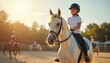 © Vadym - Young girl in helmet rides white horse during lesson at sunny equestrian school. Other children train ponies on sand arena. Outdoor animal sport activity for kids.