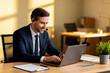 © Olha Ye - man with a hearing impairment using speech-to-text software on laptop, natural light on his face, blurred office background, inclusive modern business atmosphere