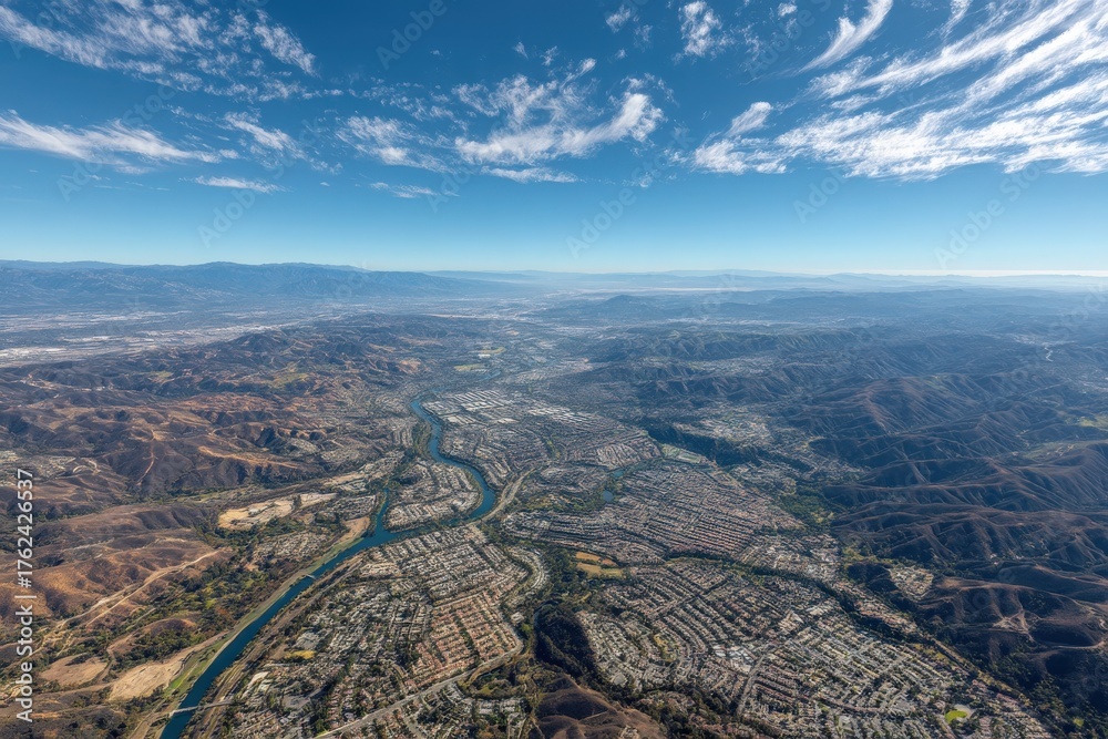 An expansive aerial view of a valley with a river winding through a suburban area. The mountains in the background highlight the natural beauty of the region under a clear blue sky.