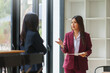 © Crystal - Businesswomen conversing in an office setting. One woman is gesturing while holding documents, discussing with her colleague