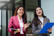 © Crystal - Two cheerful Asian businesswomen colleagues discussing work and collaborating outdoors, holding a tablet and a clipboard