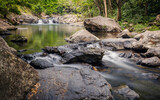 Water cascades between rocks in this long exposure shot of a peaceful gorge with pools and cascades surrounded by rainforest at Crystal Cascades in Cairns in tropical North Queensland, Australia.