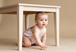 © smth.design - Curious baby in pastel outfit crawling under wooden table on neutral background with natural light and playful expression
