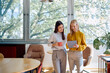 © we.bond.creations - Two businesswomen standing in an office, holding a coffee cup and looking at a tablet together during a break