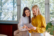 © we.bond.creations - Two smiling businesswomen discussing work and sharing ideas while looking at a digital tablet at the modern office
