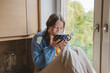 © Westend61 - Girl drinking hot chocolate near window at home