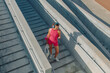 © makedonski2015 - Woman in pink athletic outfit using phone while walking down outdoor stairs in a sports area