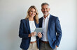 © Pete - Two business professionals smile at camera. They wear suit jackets. Woman and man stand together holding tablet. They look successful and professional. Photo suitable for business or marketing.