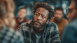 © EUT - Pensive Black man with beard listens in group, wearing plaid shirt. Show audience engagement, diversity, or attentive listening during meeting.