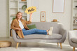© Pixel-Shot - Young woman holding speech bubble with word HELLO on sofa at home