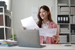 © Wasan - Asian businesswoman comparing printed documents with data on laptop screen.