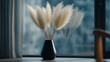 © Sawera - Pampas grass in a black vase sits near a window with a curtain and a partial view of a chair