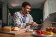 © Miljan Živković - Man working on laptop at home during breakfast