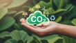 © MstTasmiya - Reducing CO2 Emissions and Promoting Sustainability Concept. A hand holds green CO2 cloud icon with environmental symbols, such as solar, wind turbines, and recycling. Reduce carbon and go green.