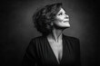 © whitestorm - A classic monochrome portrait of a mature woman with curly hair looking upwards, a serene and thoughtful expression on her face against a dark studio backdrop.