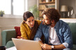 © Stockphotodirectors - A couple appears to be having a serious conversation about financial problems while seated on a green couch in their cozy living room, using a laptop to review information.