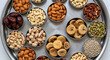 © Rayan - Overhead view of assorted dry fruits and nuts arranged in metal bowls on a round steel tray, includes almonds, cashews, figs, pistachios, dates, and seeds.