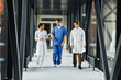 © LIGHTFIELD STUDIOS - Three multicultural doctors collaborate in a modern healthcare facility hallway