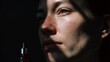 © Mitchell - Close-up of a person's face with dramatic lighting, holding a dropper bottle of amber liquid, suggesting skincare or wellness.