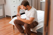 © Marina Demidiuk - Handsome man cutting nails wear white t-shirt sitting at home light bedroom. Guy clipping fingernails doing hygiene procedure, grooming body. Self care. Softly lit indoor space. Male morning routine.