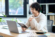 © LIGHTFIELD STUDIOS - Handsome young man working on a laptop while reviewing notes in a bright office space